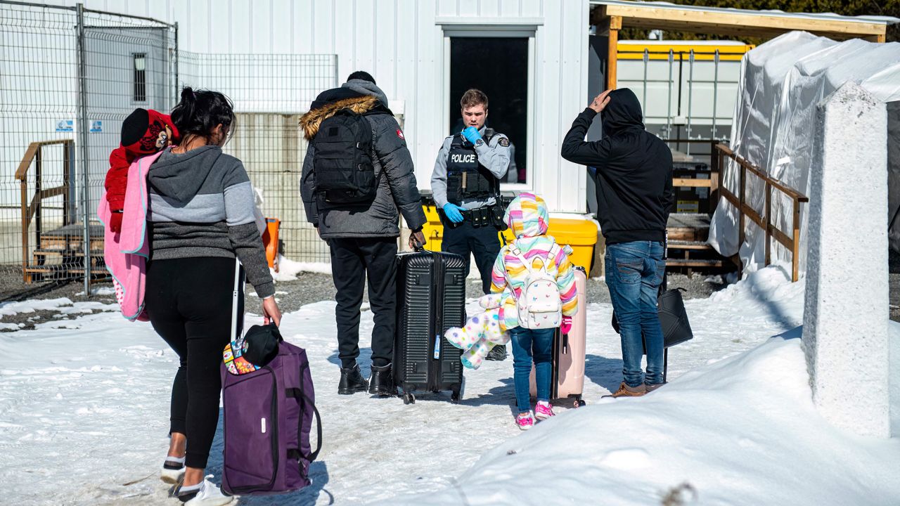یک افسر در 3 مارس 2023 با مهاجران هنگام رسیدن به گذرگاه مرزی Roxham Road در Roxham، کبک، کانادا، صحبت می کند.
